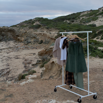 clothes hanging on clothing rack on wheels with a sandy-beach background 