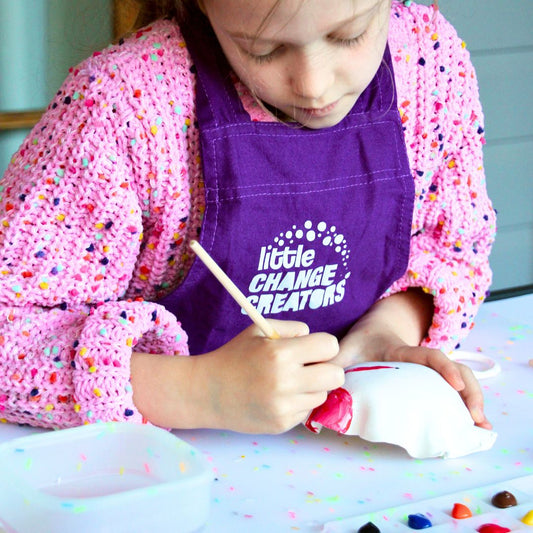 A girl wearing a Little Change Creators apron as she paints a clay piece.