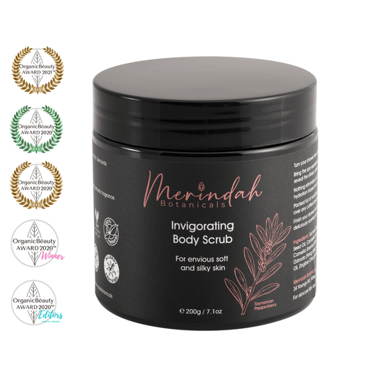 A 200g black jar of Merindah Botanicals' Invigorating Body Scrub, adorned with a floral design on the label, contains an all-natural exfoliating body scrub. Award badges on the left highlight its recognition from Organic Beauty Awards between 2020 and 2021.