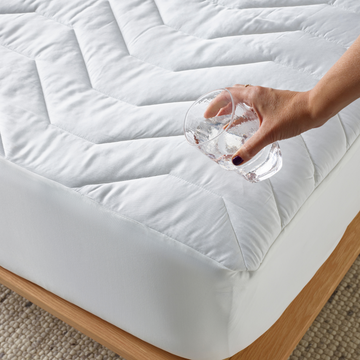 Hand pouring water over a mattress protector